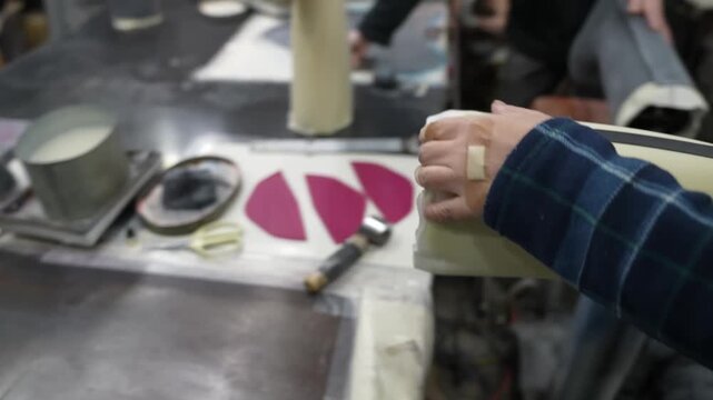 Close up of hands smoothing a black rubber trim strip along the length of a boot last on a workbench
