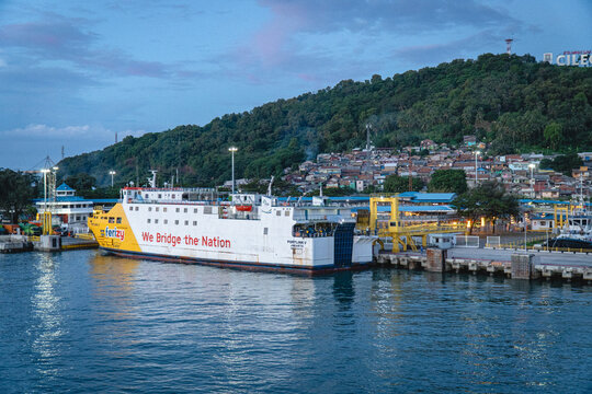 Cilegon, Indonesia - August 20, 2026: A passenger ferry is docked at Merak Port, with a green hillside and waterfront buildings visible in the background.