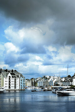 Historic Brosundet canal under dramatic cloudy sky in Alesund, Norway. Beautiful waterfront Art Nouveau architecture and docked boats along Brosundet canal in Alesund, Norway.