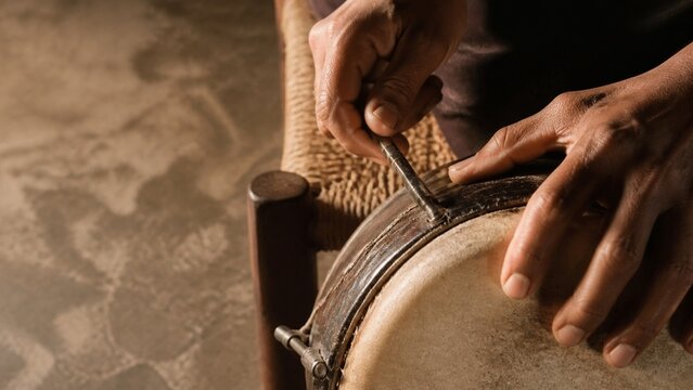 Close up view of hands working on a traditional drum surface, suggesting craftsmanship and music making, perfect for cultural or artistic projects, evokes rhythm and heritage