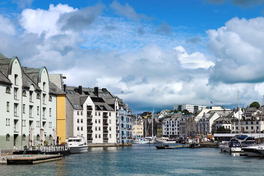 Beautiful waterfront Art Nouveau architecture and docked boats along Brosundet canal in Alesund, Norway. Contrast of blue sky and heavy storm clouds over the historic Brosundet canal.