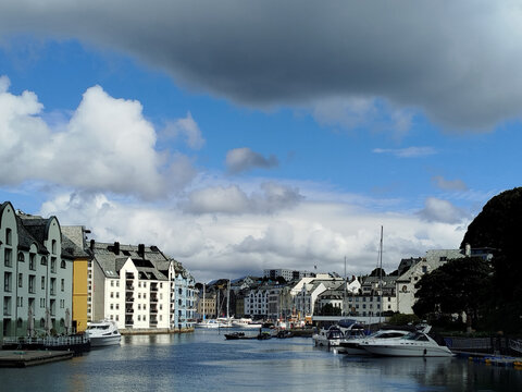 Beautiful waterfront Art Nouveau architecture and docked boats along Brosundet canal in Alesund, Norway. Contrast of blue sky and heavy storm clouds over the historic Brosundet canal.