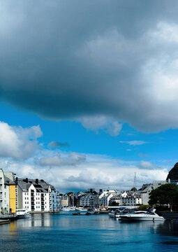 Historic Brosundet canal under dramatic cloudy sky in Alesund, Norway. Beautiful waterfront Art Nouveau architecture and docked boats along Brosundet canal in Alesund, Norway.