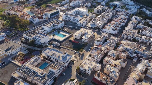 Aerial view of coastal resort town with white buildings and blue swimming pools at sunset.