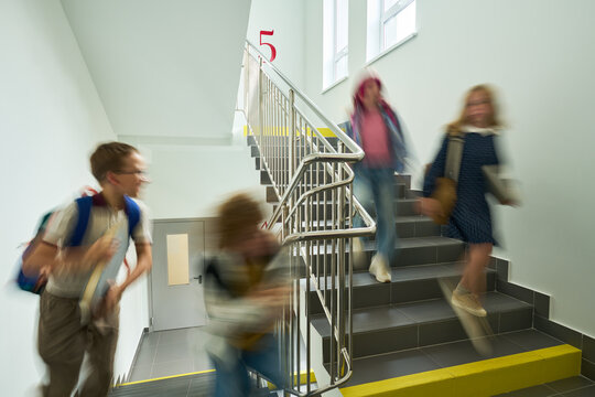 Caucasian kids running down school stairs with motion blur, representing active student life. Image ideal for educational marketing, school safety campaigns, and youth lifestyle promotions