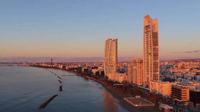Stunning aerial view of limassol coastline at sunrise, with modern high-rise buildings reflecting golden light.