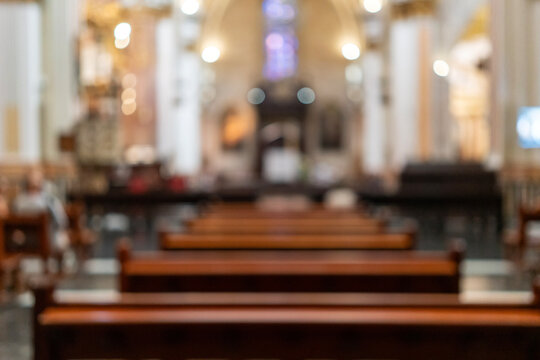 Blurred interior view of a classic European church cathedral with wooden pews, stained glass windows, elegant arched ceiling architecture, and warm indoor bokeh light for background design copy space