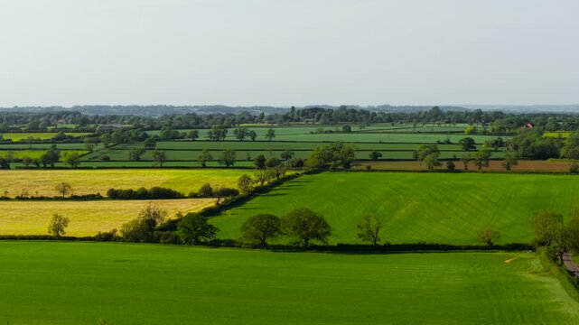 Patchwork farmland agricultural landscape rural fields. Fertile crop acreage bordering hedgerows and scattered trees beneath bright spring sky. Sustainable countryside land use and growing cereals