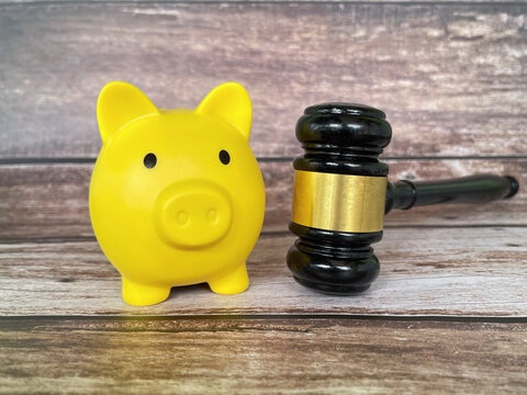 Yellow piggy bank and wooden judge gavel on a rustic background, symbolizing financial responsibility, debt, savings, law, and economic decisions.