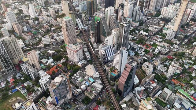 Aerial view of bangkok city downtown at sunrise with skytrain passing by, modern buildings and crowded residential areas in motion.