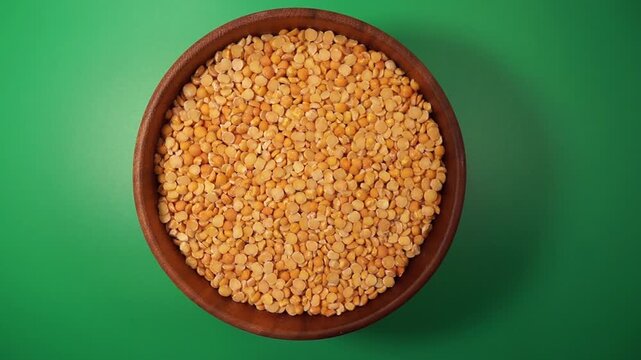 Rotation of split peas in a wooden bowl on a green background. Top view
