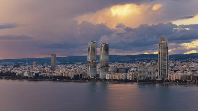 Aerial view of Limassol city skyline during sunset with modern skyscrapers and dramatic clouds over Mediterranean sea.