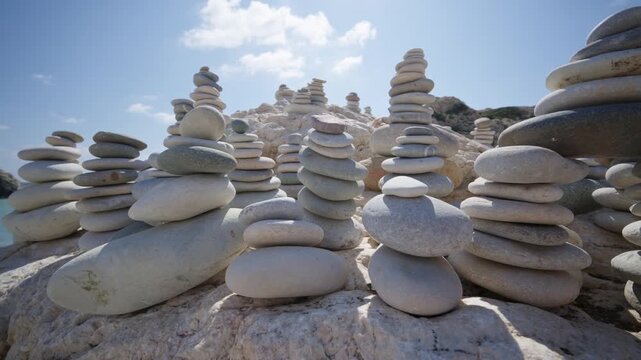 Zen stone towers on white rock by turquoise sea water against bright blue sky and sun.
