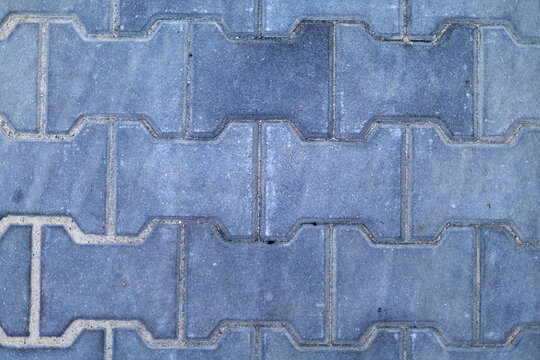 Gray Interlocking Concrete Paving Stones Pattern. Close-up top view of gray interlocking concrete paving stones forming a repeating geometric pattern with visible joints and light surface wear.