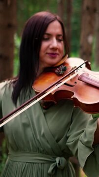 Woman in flowing green dress playing violin in tranquil forest, emotional outdoor performance captured in close-up and mid-shot frames of serene musician