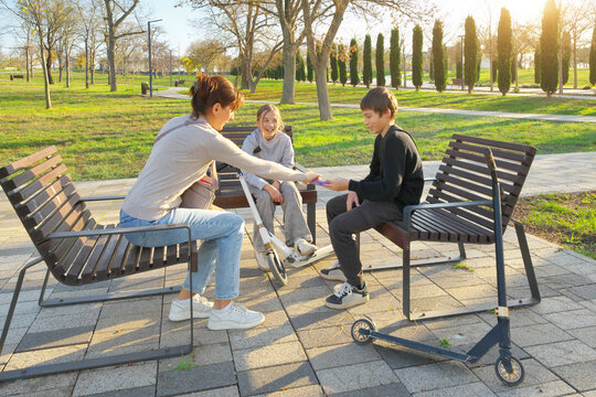 Mother giving chocolate bar and her son while sitting on benches with scooters in an autumn park. Family financial literacy scene