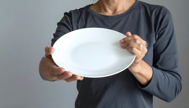 Person Holding an Empty White Ceramic Plate Representing Hunger, Starvation, or Dietary Restrictions