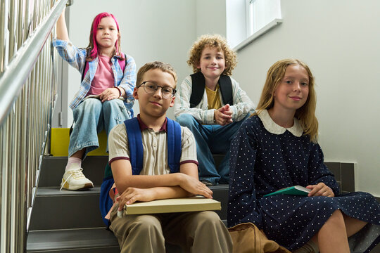 Portrait of diverse Caucasian school kids sitting on stairs with backpacks and books. Group of happy children looking at camera, representing primary education and school enrollment campaigns