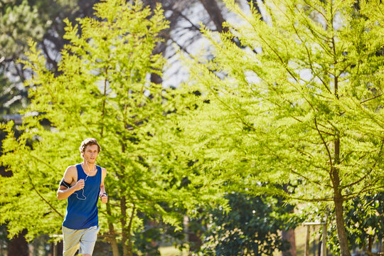 Man, earphones and running in park for fitness, exercise or streaming music with cardio wellness. Athlete, jogging and outdoor with tech for radio, training tips podcast or challenge for heart health