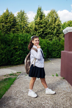 Schoolgirl walks along a pathway by green trees as she gets ready for a new school year. She carries a backpack and thinks
