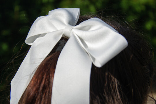 Schoolgirl ties her hair back with a white bow as she gets ready for school. Trees are visible in the background