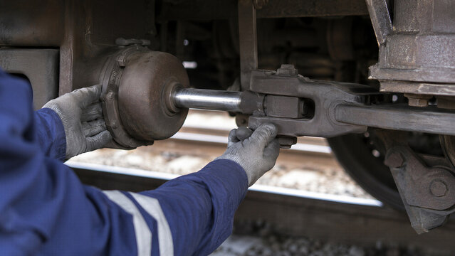 Railway technician inspecting and maintaining a freight train coupling and mechanical undercarriage component. Industrial rail safety, repair, engineering and transportation infrastructure concept