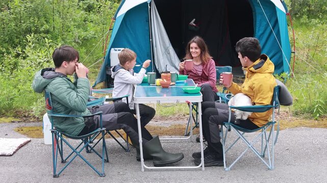 Happy family with children, eating breakfast in the morning in front of a tent, wild camping in nature, Norway, morning, sunny morning