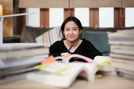 Portrait, Asian teenage girl, cheerful, learning at home with pile of books, smiling with stack of textbooks, reading and writing, self-study for school, Homeschooling, university education lifestyle.