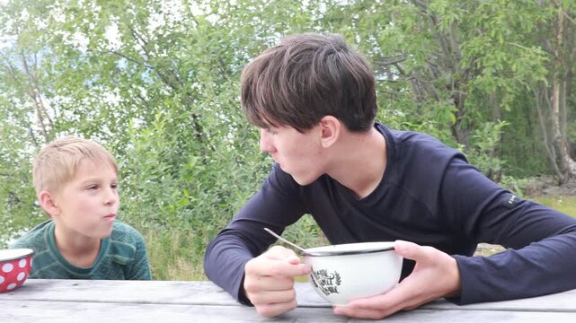 Children, boy brothers, having lunch in a reststop in Norway in beautiful nature. Kid with teddy bear eating lunch on a public wooden bench while on camping holiday in Norway, Lofoten