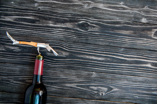 glass wine bottle and corkscrew on wooden background top view