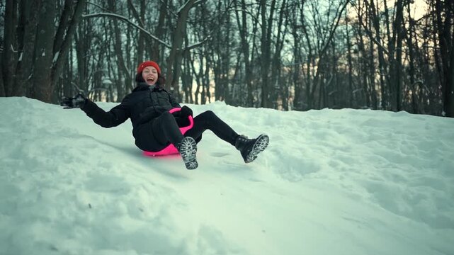 cheerful smiling young woman sledding on snow saucer downhill in winter, outdoor fun and active winter recreation 4k