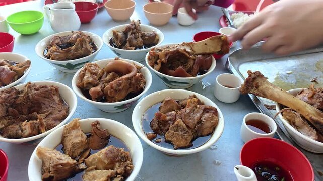 Worker serving authentic and original Klang bak kut teh herbal stewed pork in multiple small bowls. Each bowl consist of different pork parts.