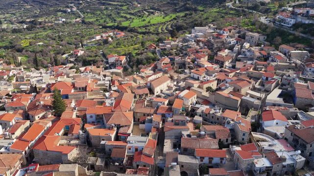 Aerial view over a picturesque cyprus village with traditional houses nestled in a lush green valley, showcasing mediterranean architecture and vibrant landscape under bright sunlight.