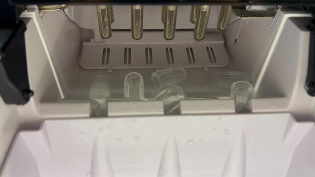 Inside a portable electric ice maker machine, freshly formed bullet-shaped ice cubes automatically drop from the freezing metal rods into the collection tray