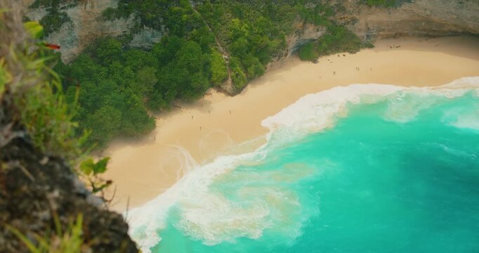 Turquoise ocean water meets the white sand beach at the base of steep cliffs in Nusa Penida