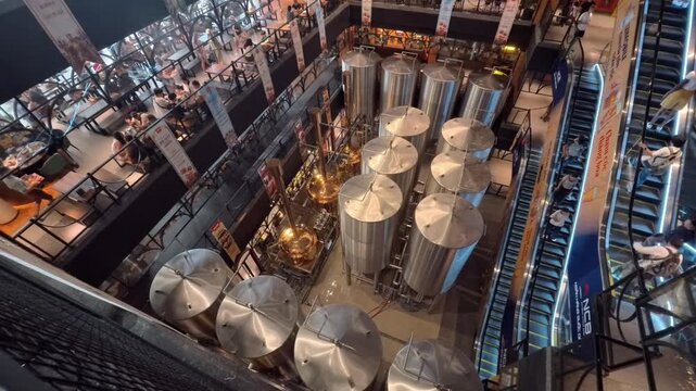 A wide interior view of the Bana Brew House at Ba Na Hills. The ground floor features large stainless steel and copper brewing vats, while others host patrons dining in a industrial-style atmosphere.