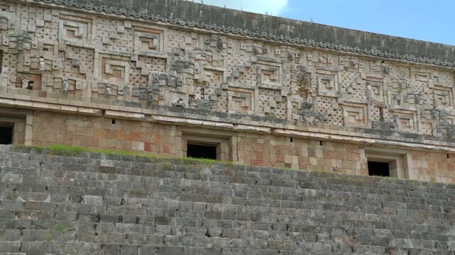 Static wide shot of the intricate Puuc style stone facade and stairs of the Governor Palace at Uxmal archaeological site in Yucatan, Mexico.