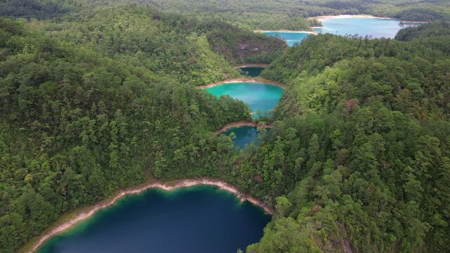 Slow aerial drone forward shot revealing a chain of turquoise and deep blue crater lakes nestled in forested hills at Montebello, Chiapas, Mexico.