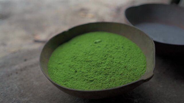 Static close up shot of fine green mambe powder inside a traditional gourd bowl on the floor inside an Amazonian maloca in Colombia.