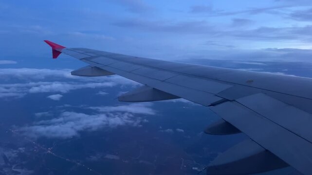 As the journey progresses into the late evening twilight the passenger plane cruises smoothly above the scattered clouds revealing glowing city lights far below under the serene and beautiful blue sky