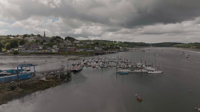 A wide aerial shot of the Crosshaven boat marina and colorful village houses under a cloudy sky in Ireland. Suitable for travel and maritime industry content.