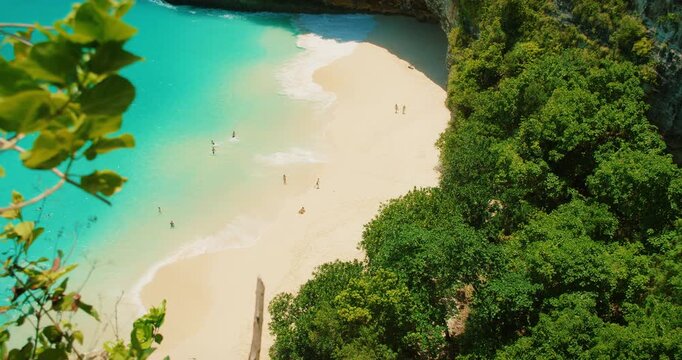 People walking and swimming on pristine white sand beach by tropical ocean water