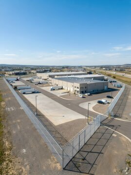 Aerial view of a modern industrial warehouse complex with delivery trucks, secured perimeter, highway, and open landscape. Logistics, manufacturing, and commercial development concept.