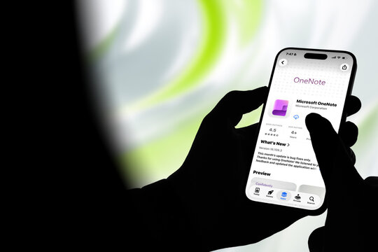 Kiel, Germany - 08-20-2026: Smartphone displaying the OneNote note-taking and organization app in the App Store, held by silhouetted hands with blurred background