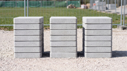 Fototapeta premium Gray concrete paving blocks stacked in three columns on gravel at a construction site outdoor