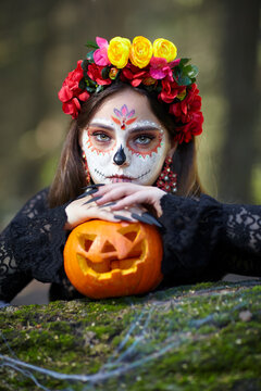 Halloween beauty portrait of young woman with Halloween pumpkin lies on a tree trunk in the forest.