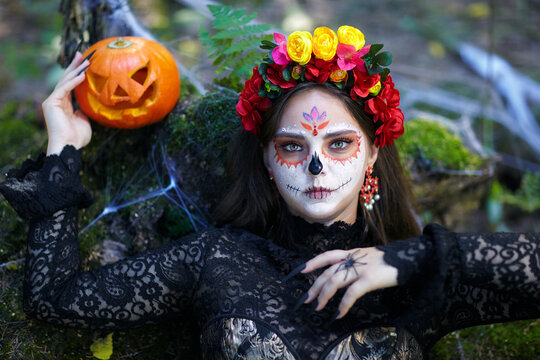 Halloween beauty portrait of young woman in the forest on a mossy stump with a halloween pumpkin.