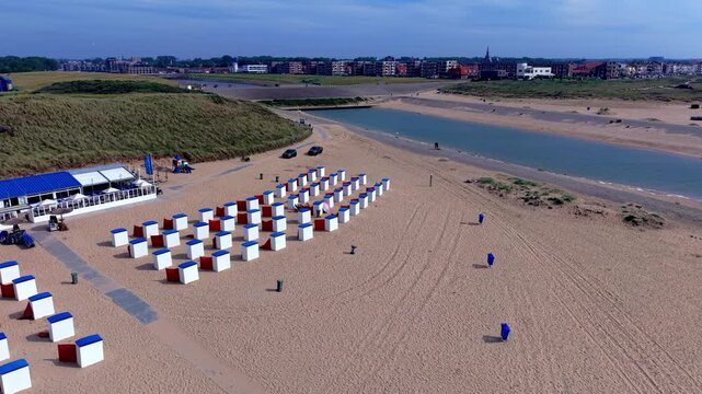 High angle horizontal aerial drone video clip of beach cabins, river mouth outlet, sand dunes, pavilion, and Katwijk aan Zee town skyline, South Holland, Netherlands, West Europe
