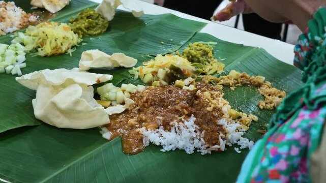 Closeup of hand and finger mixing rice with curry served on banana leaf, popular Indian food in restaurant in Malaysia. Eating with hand is culturally common within the Indian community.