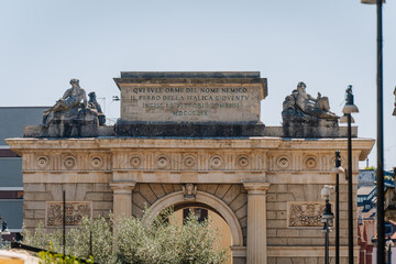Fototapeta premium Historical arch monument with sculptures and inscriptions in Milan, showcasing classical architecture and decorative elements in a public square
